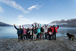 Lake Whakatipu Queenstown swimming group standing beside the lake and waving their arms happily