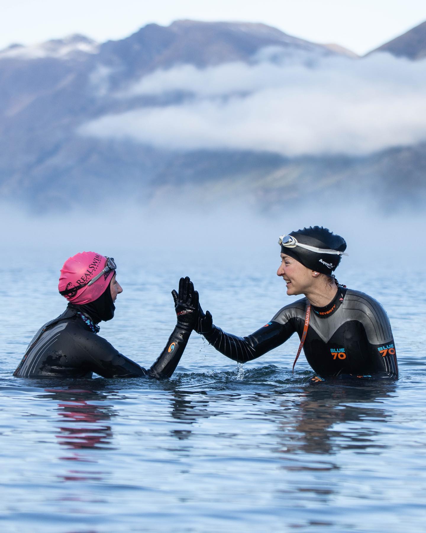 Two open water swimmers in wetsuits giving each other a high-five. Image by Connor Paton