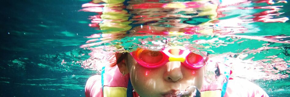 Child learning to swim wearing life jacket, underwater and blowing bubbles