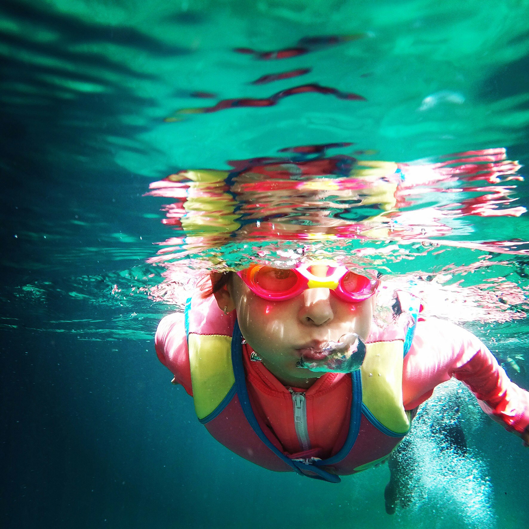 Child learning to swim wearing life jacket, underwater and blowing bubbles