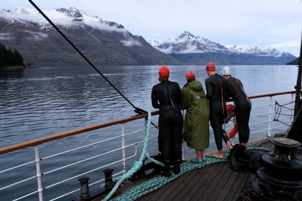 Swimmers stand on the deck of the TSS Earnslaw steamship looking out at the mountains in Queenstown