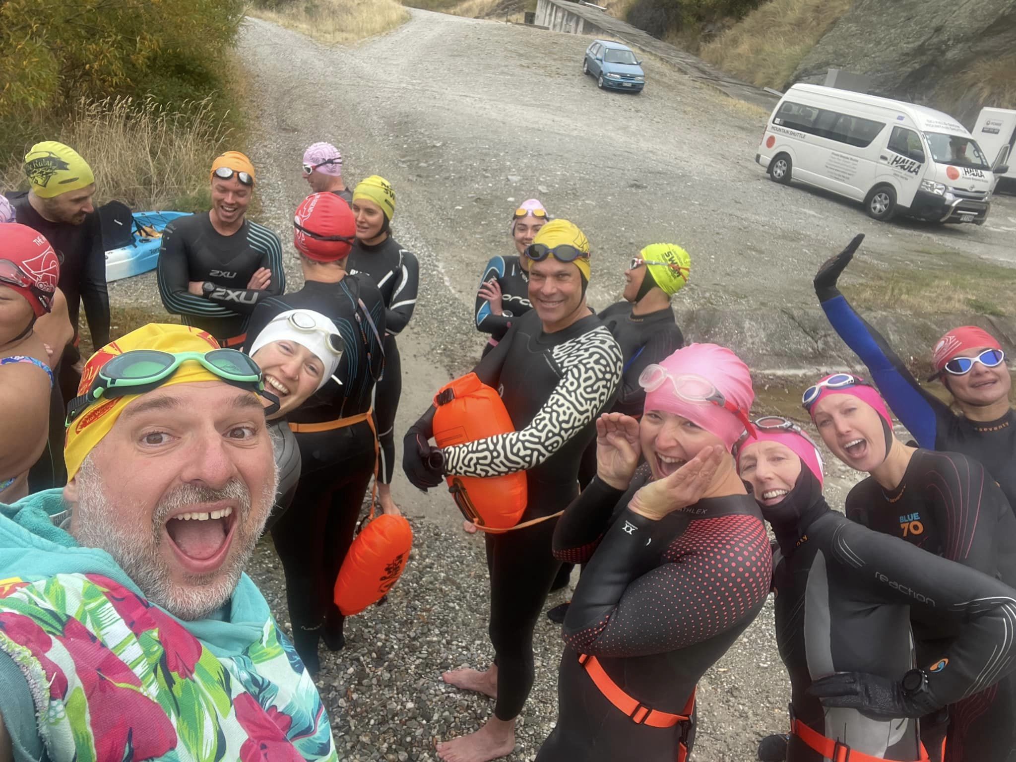 Swimmers in wetsuits smile at the camera before getting into Lake Dunstan